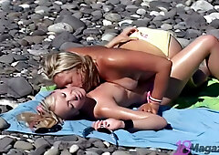 Candie Elektra and a blonde lover share intimate kisses on a sunlit rocky beach