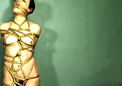 Serf Mila is restrained in unrelenting rope servitude, her body wrapped tightly from head to toe. Her legs, belly, tits, neck, and even her throat are