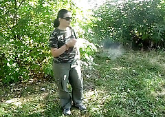 Person urinates outdoors on sandy ground in public while crouched