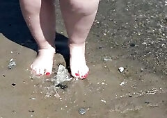 A obese woman with large feet walks along the shore.